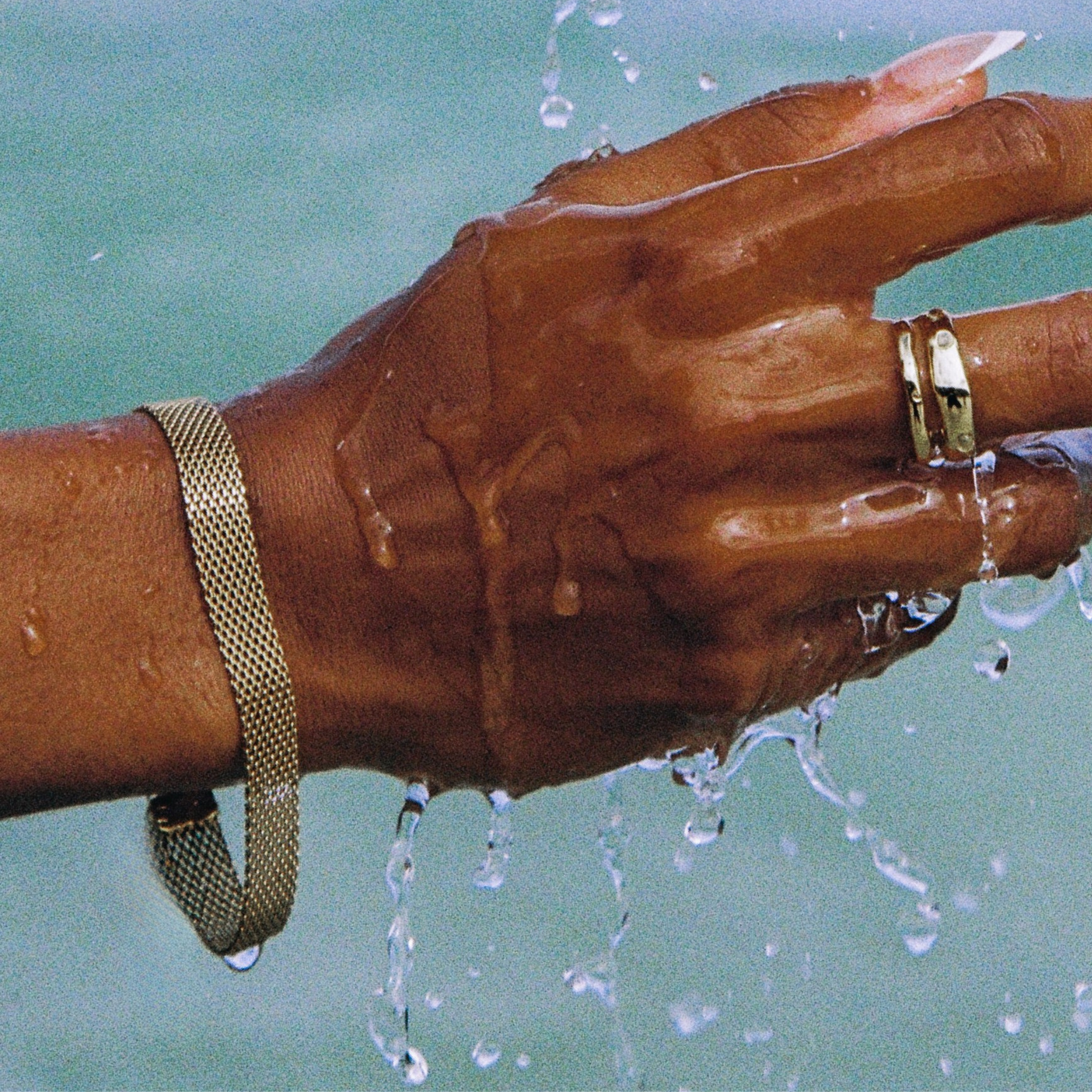 Hand with a gold ring and bracelet under running water